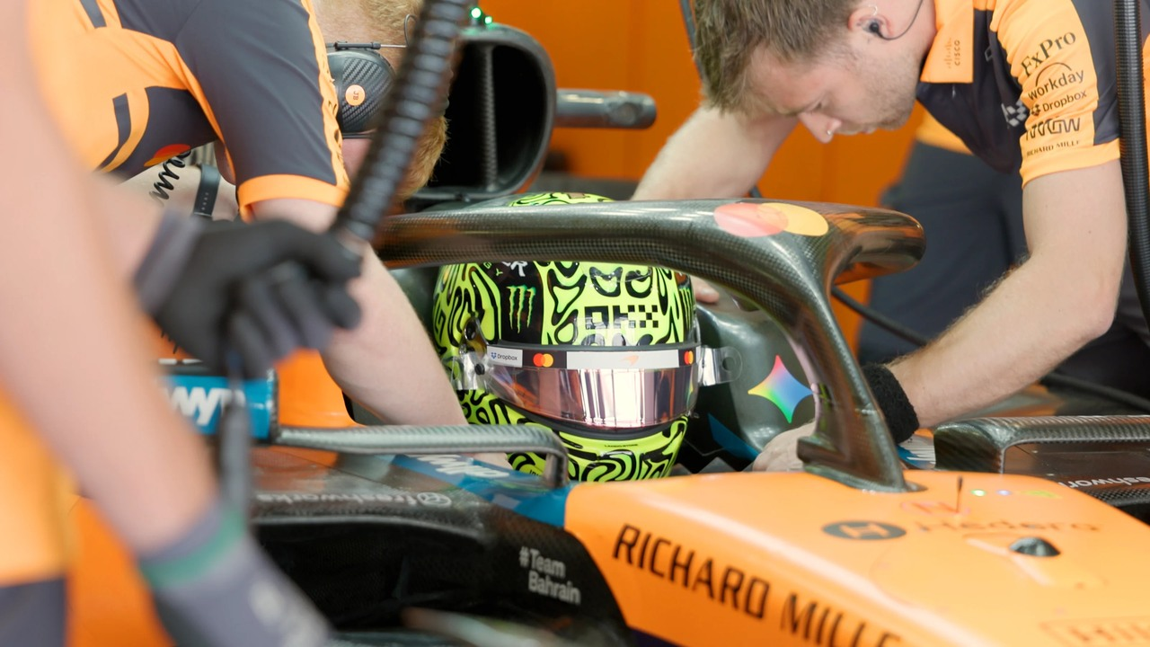 Un pilota McLaren siede nella MCL60 mentre i meccanici lavorano intorno all'abitacolo.