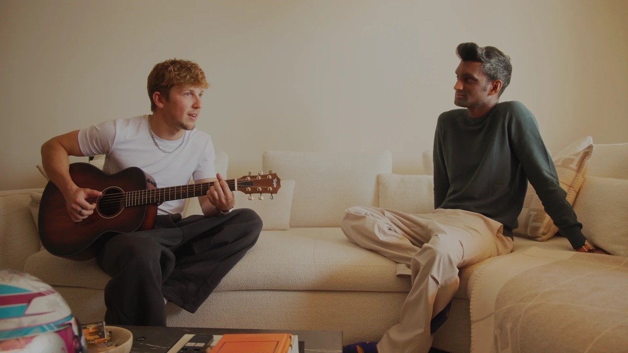 Liam Lawson holds a guitar while sitting beside another man